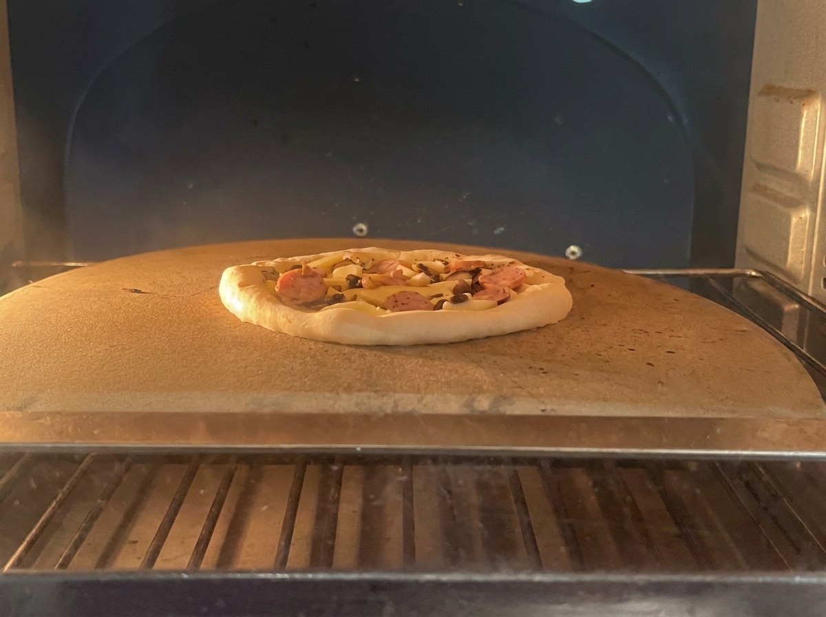 Eine unbebackene Pizza mit Salami und Pilzen liegt auf einem Backstein in einem professionellen Ofen.