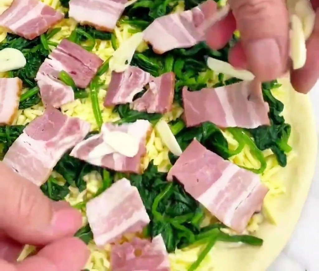 Eine Hand streut hauchdünne, fast transparente Knoblauchscheiben auf eine vorbereitete Pizza.