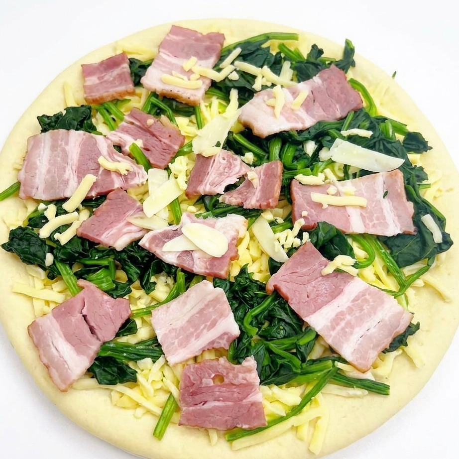 Draufsicht auf eine belegte Pizza mit Spinat, Speck und Knoblauch, die mit einer letzten Prise Mozzarella bestreut wird.