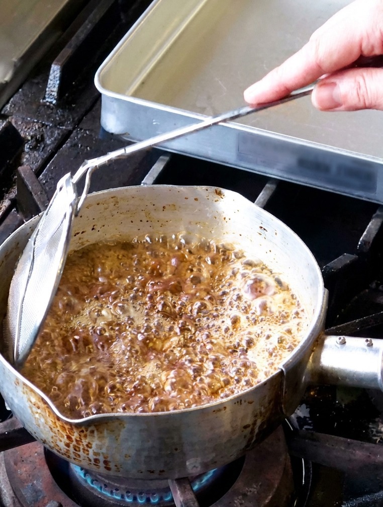 Knoblauchscheiben frittieren in einem Topf mit sprudelndem Öl, während weißer Dampf aufsteigt.