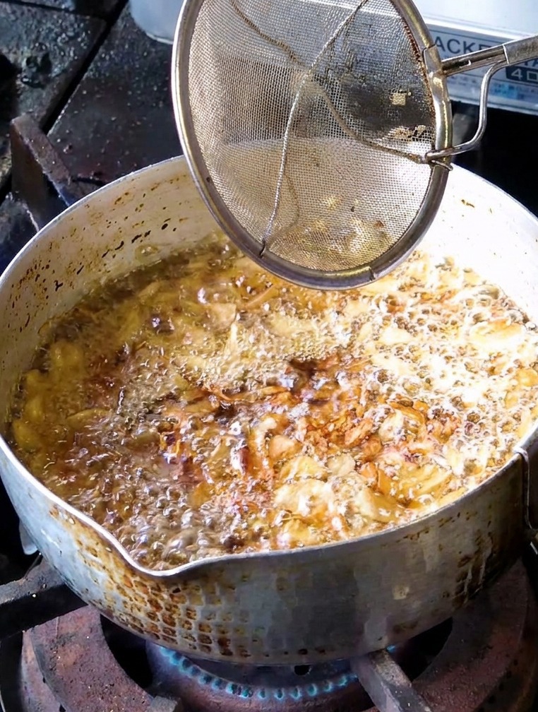 Ein feinmaschiges Sieb schöpft hellgoldene Knoblauchscheiben aus dem sprudelnden Öl.
