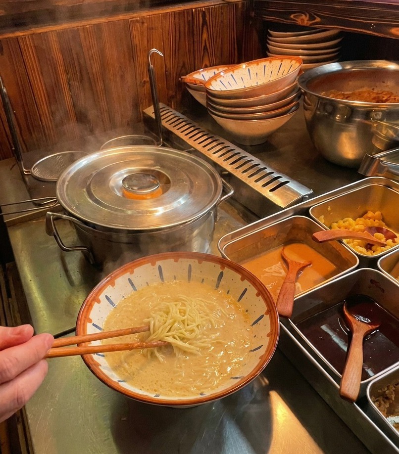 Mit Stäbchen werden gekochte Ramen-Nudeln angehoben und ordentlich in eine Schüssel mit cremiger Brühe gefaltet.