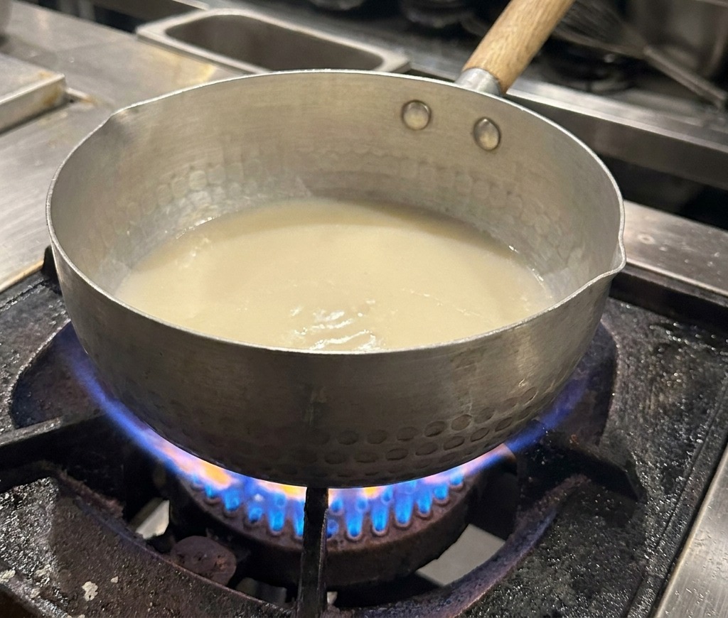 Nahaufnahme eines Topfes mit weißer Brühe, auf deren Oberfläche feine Öltröpfchen schimmern.