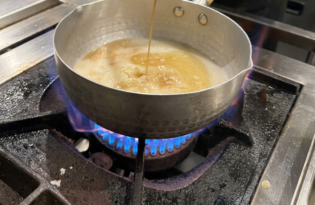 Dunkle Sojasauce wird mit einer Schöpfkelle in die helle Brühe gegossen.