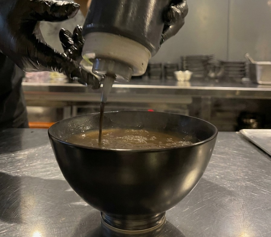 Schwarzes Öl wird aus einer Flasche in die Saucenschale geträufelt.