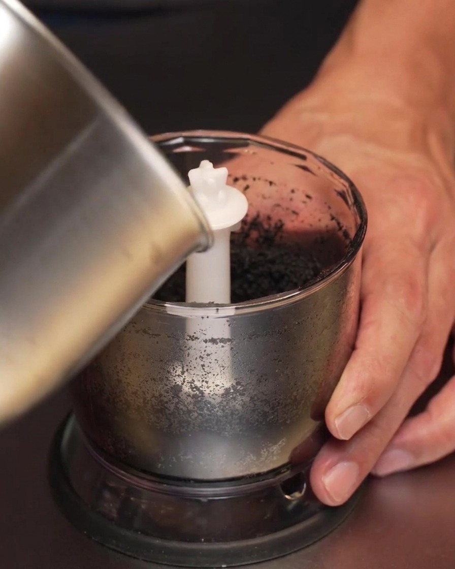 Dunkles Knoblauchöl wird aus einem Topf in einen Mixbecher mit schwarzer Knoblauchpaste gegossen.