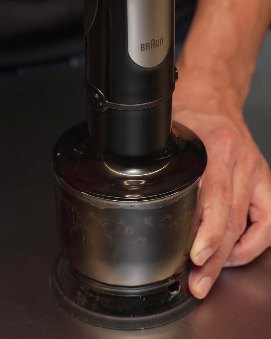 Ein Stabmixer verarbeitet Knoblauch und Öl zu einer glatten, schwarzen Flüssigkeit.