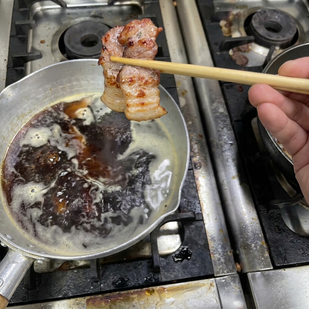 Ein Stück gebräunter Schweinebauch wird mit Stäbchen über einem Topf mit simmernder dunkler Sauce gehalten.