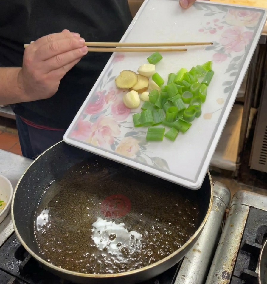 Gehackte Frühlingszwiebeln, Ingwer und Knoblauch werden von einem Schneidebrett in heißes Öl geschoben.