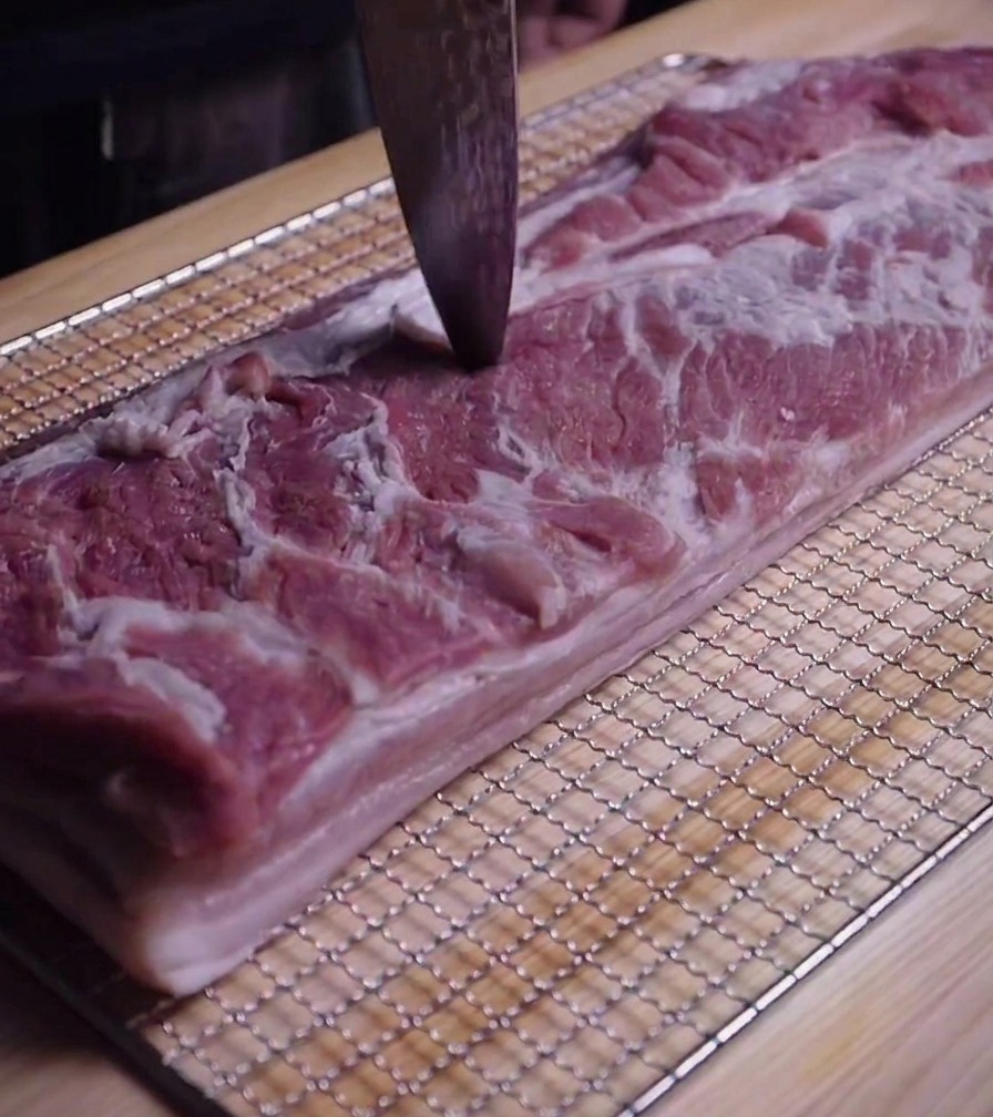 Nahaufnahme einer Messerspitze, die kleine Löcher in die Oberfläche von rohem Schweinebauch sticht.