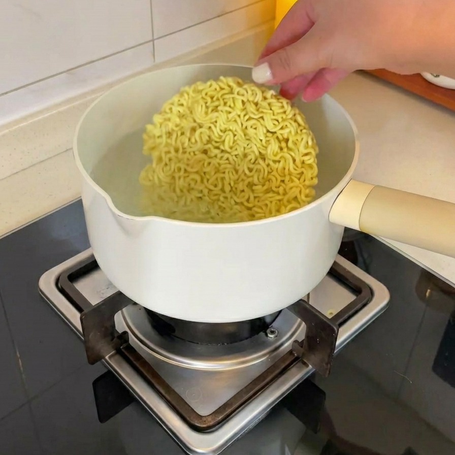 Eine Hand legt einen Block getrocknete Instant-Ramen-Nudeln in einen Topf mit kochendem Wasser auf dem Herd.