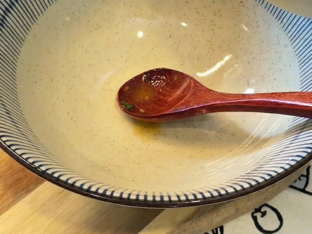 Cremige, orangefarbene Brühe wird aus einer kleinen Schüssel in eine große blau-weiß gestreifte Keramikschüssel gegossen.