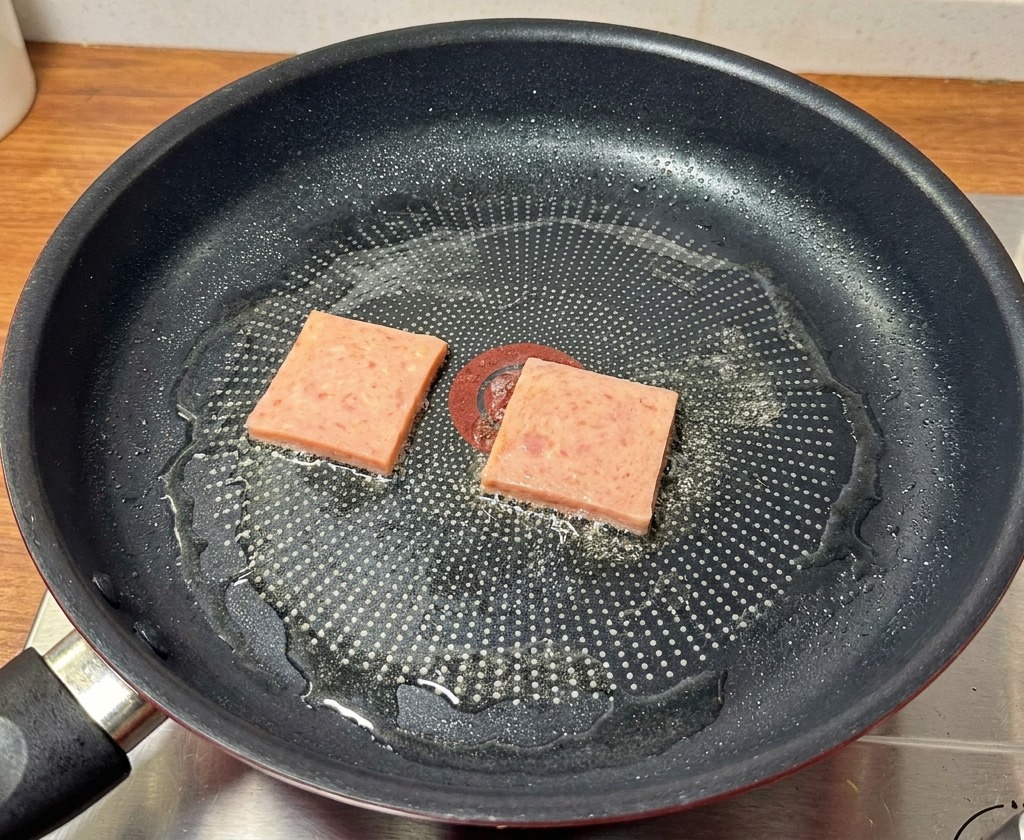 Scheiben von Frühstücksfleisch werden in einer schwarzen Pfanne goldbraun angebraten.
