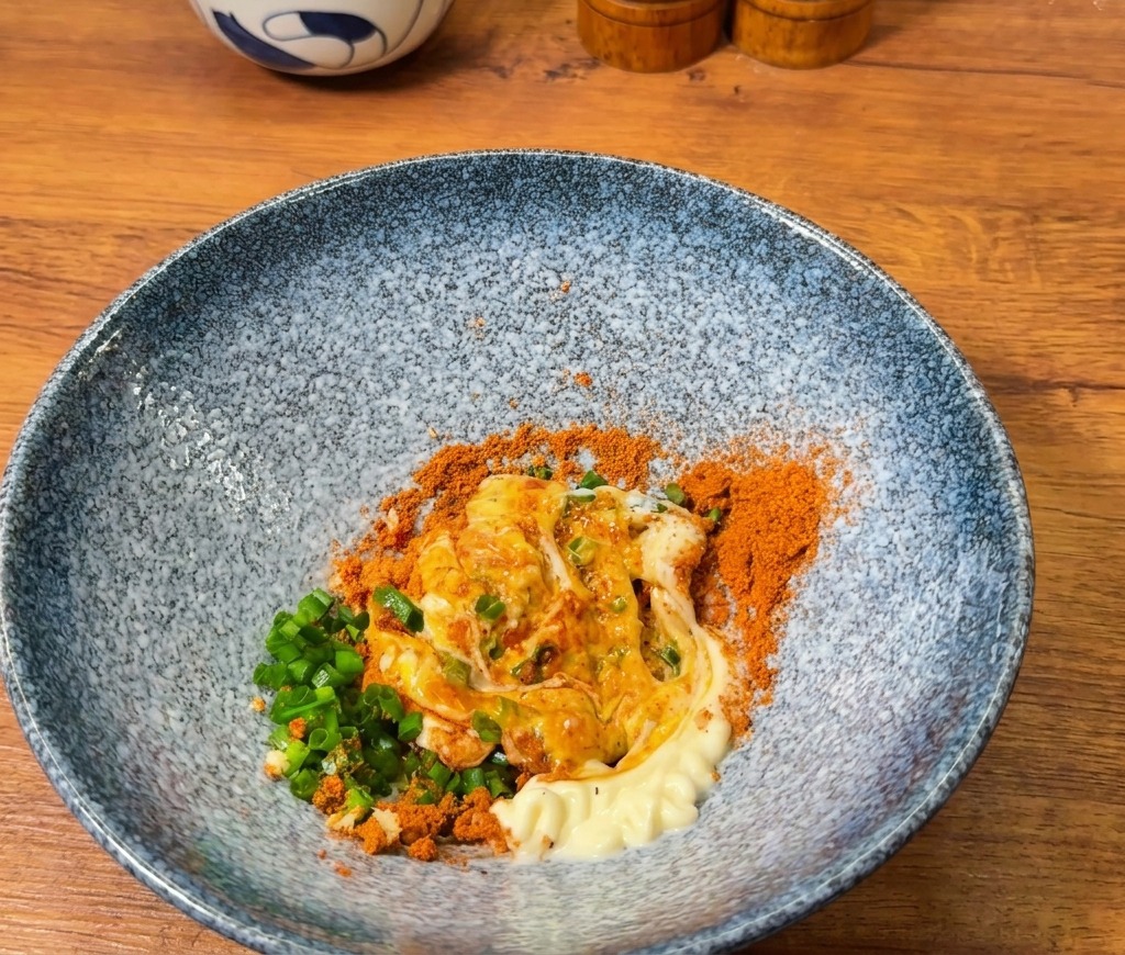 Eine orangefarbene Würzmischung wird in einer blauen Schale mit einem Klecks weißer Mayonnaise vermengt.