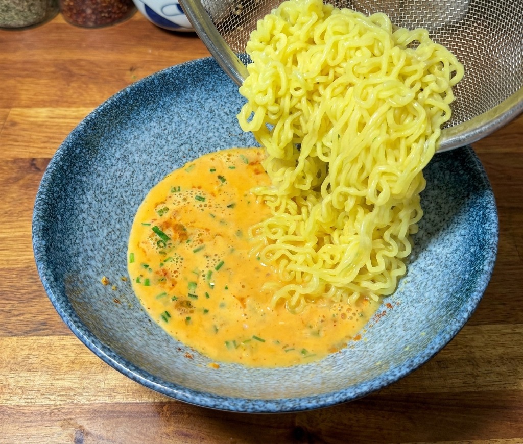 Gekochte Ramen-Nudeln werden aus einem Sieb in die Schüssel mit der cremigen Brühe gegeben.