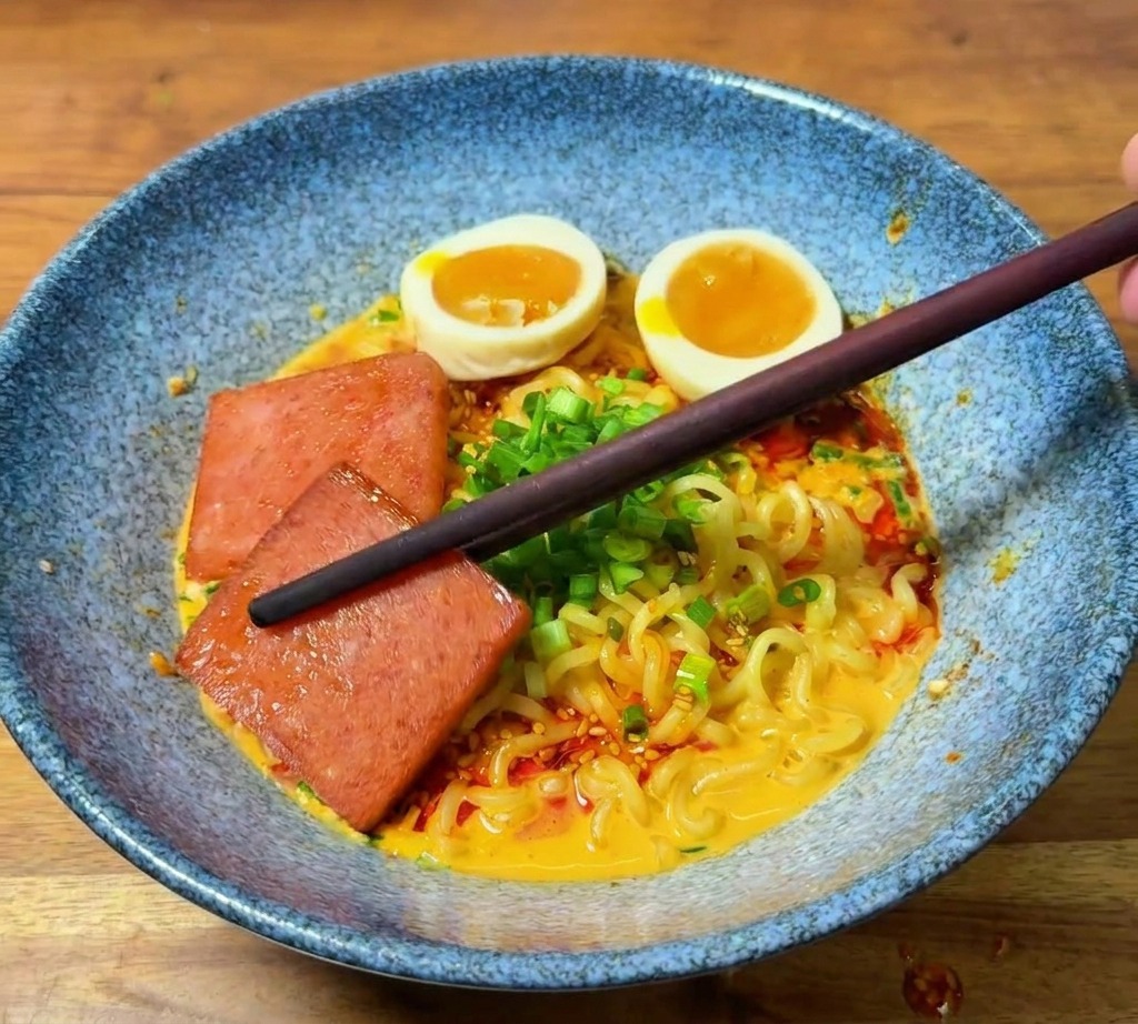 Stäbchen platzieren eine Scheibe gebratenes Frühstücksfleisch in der Ramen-Schüssel.