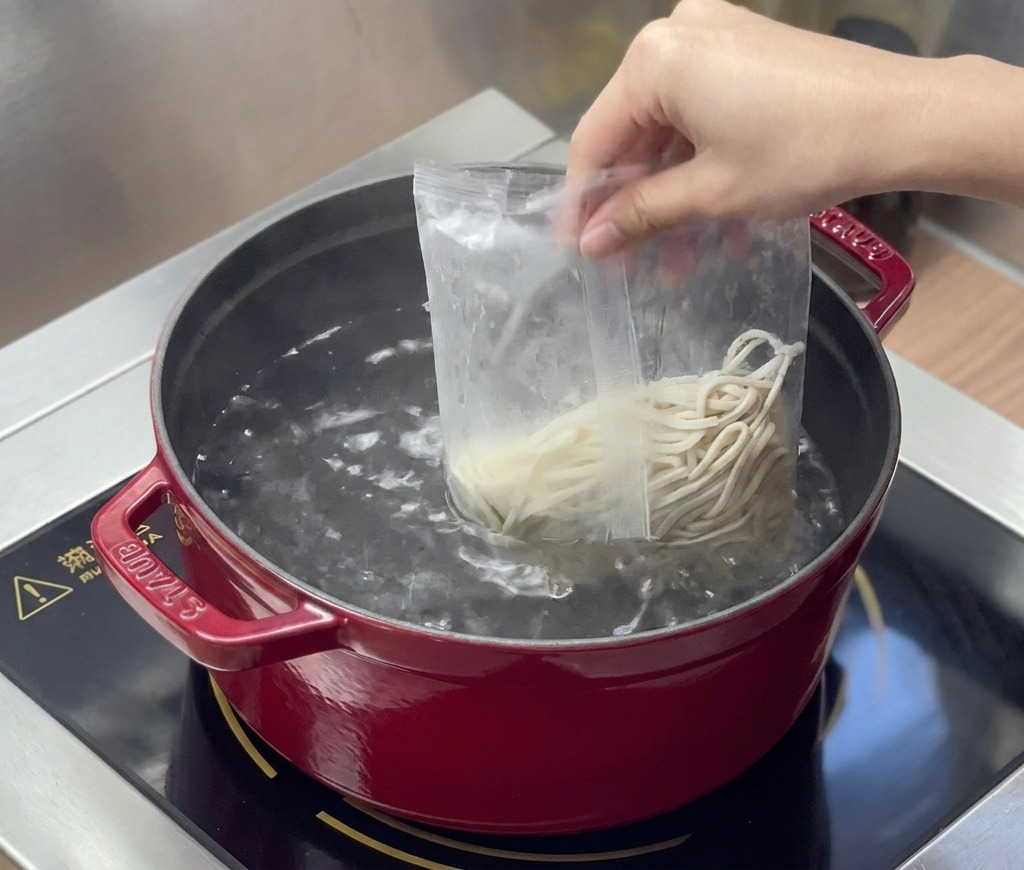Frische Ramen-Nudeln werden aus einer Plastikverpackung in einen Topf mit kochendem Wasser gegeben.