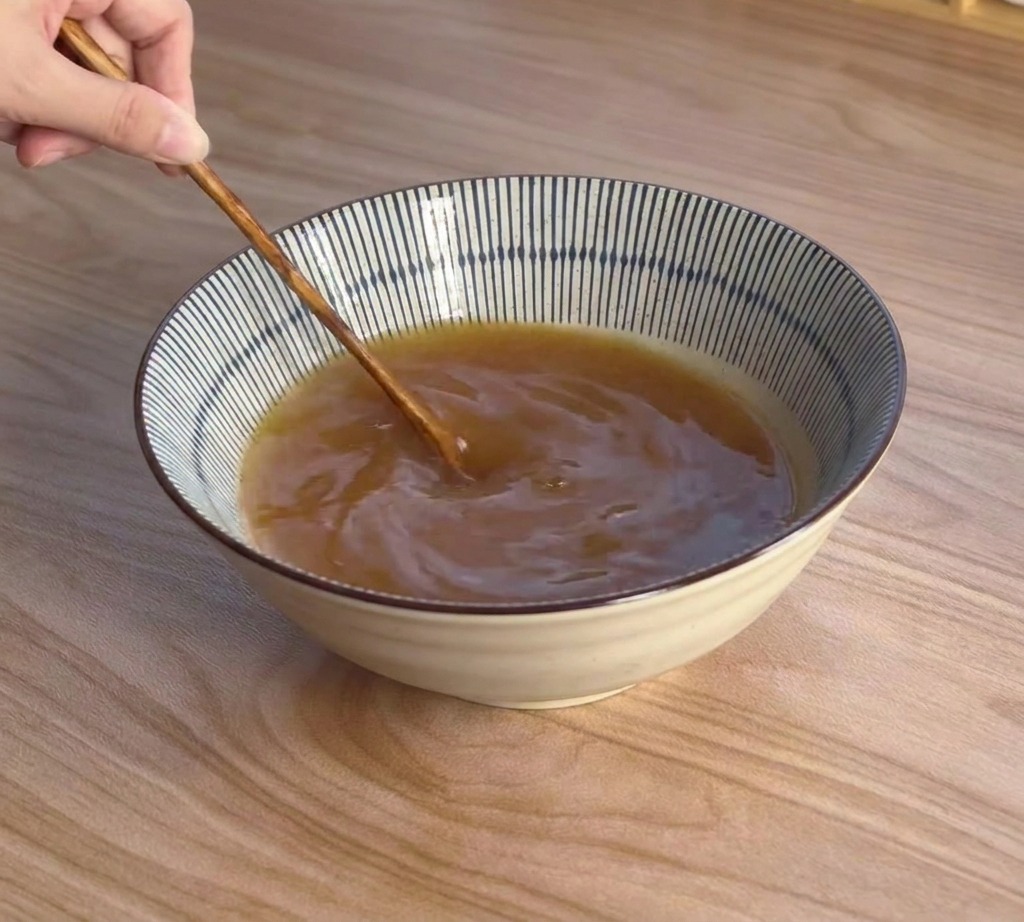 Ein Holzlöffel rührt die bräunliche Miso-Brühe in einer blau-weißen Keramikschüssel glatt.