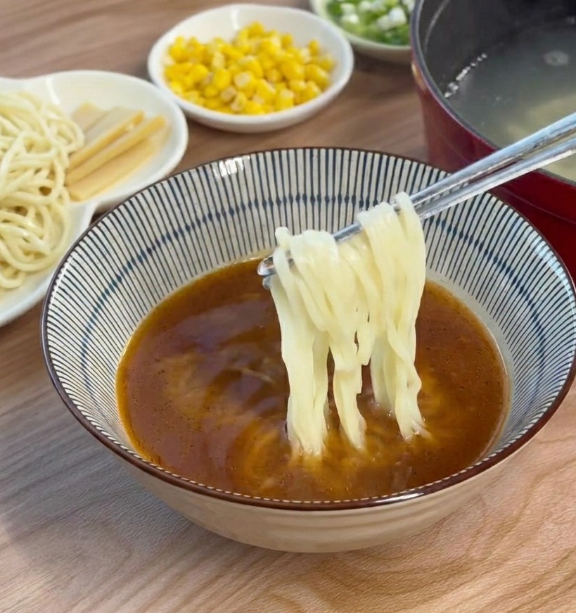 Gekochte Ramen-Nudeln werden mit Stäbchen in die braune Miso-Brühe gegeben und untergehoben.