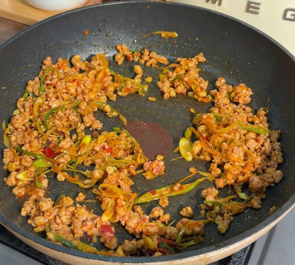Hackfleisch und Frühlingszwiebeln werden in einer dunklen Pfanne angebraten, bis das Fleisch gar und gebräunt ist.