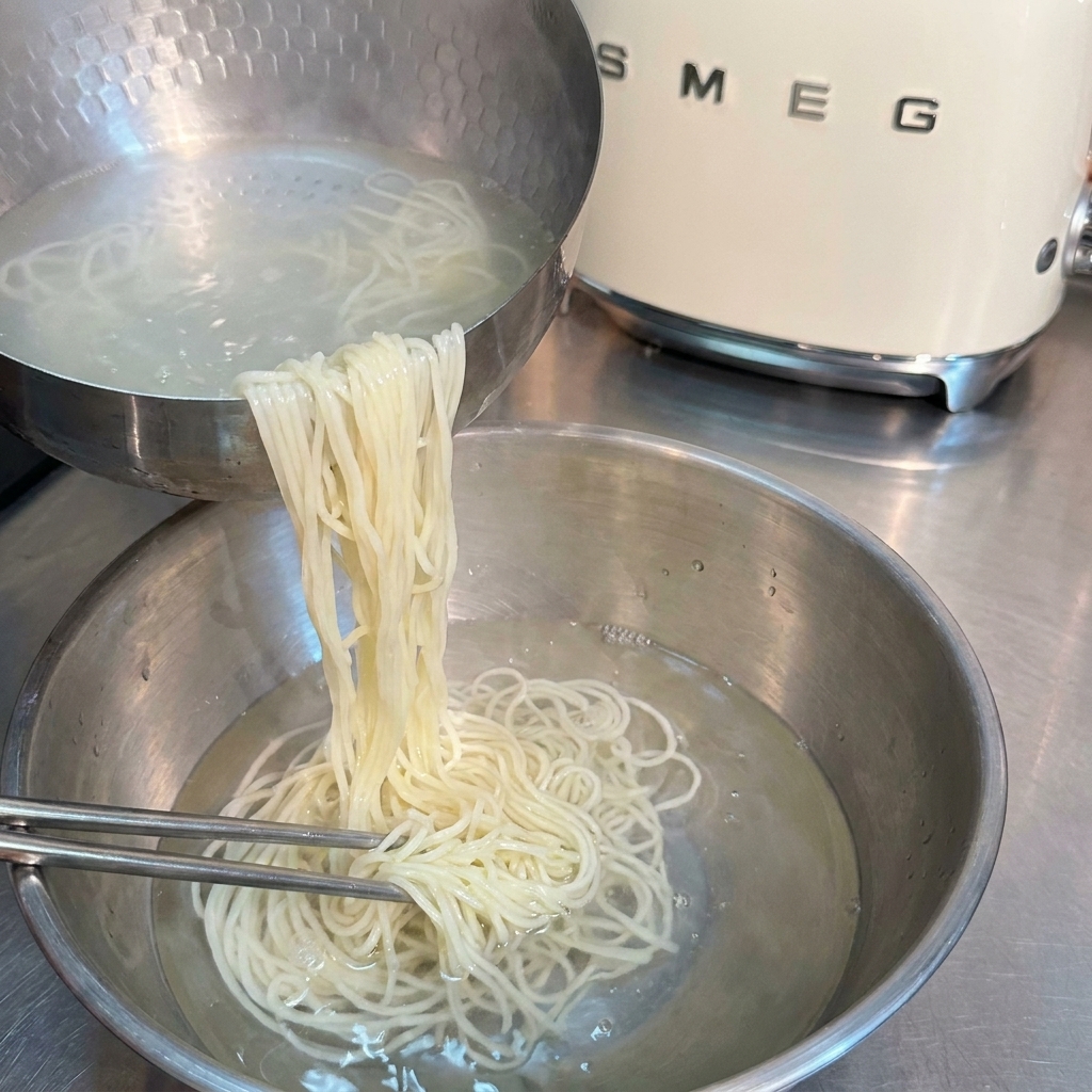 Gekochte Ramen-Nudeln werden mit Metall-Essstäbchen in einer Schüssel mit kaltem Wasser abgeschreckt.