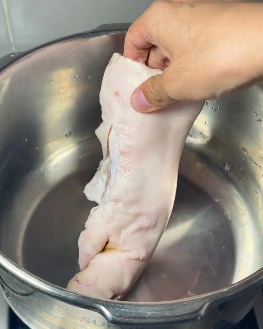 Eine Hand legt einen rohen Schweinefuß, einen großen Markknochen und mehrere Hühnerfüße in einen Edelstahltopf.
