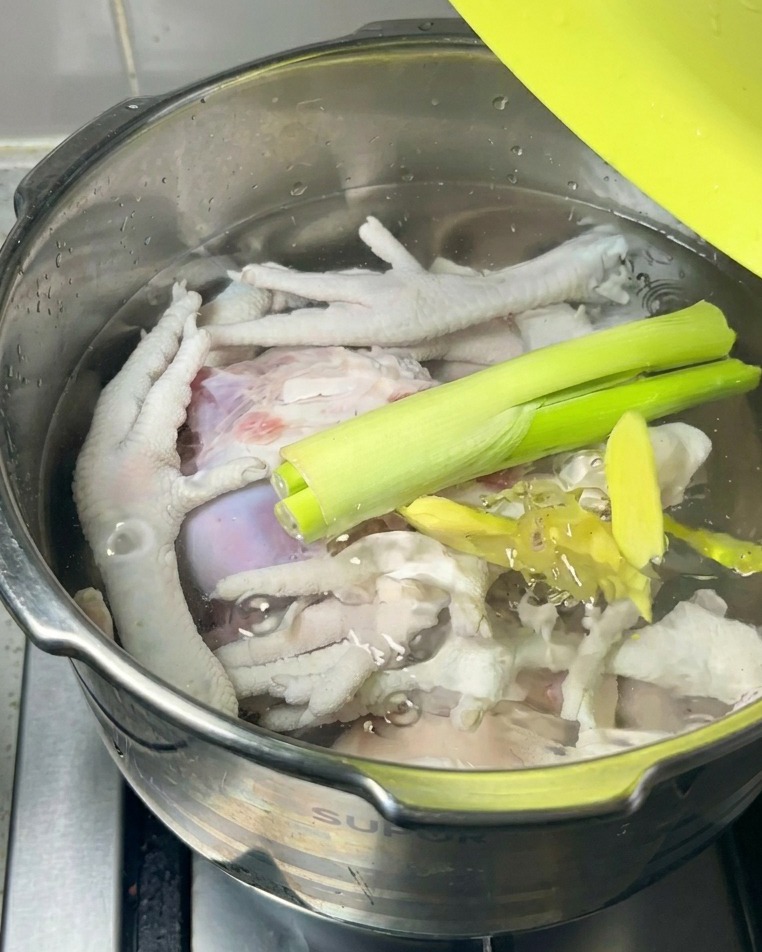 Frische Frühlingszwiebeln und Ingwerstücke liegen auf dem rohen Fleisch und Wasser im Kochtopf.