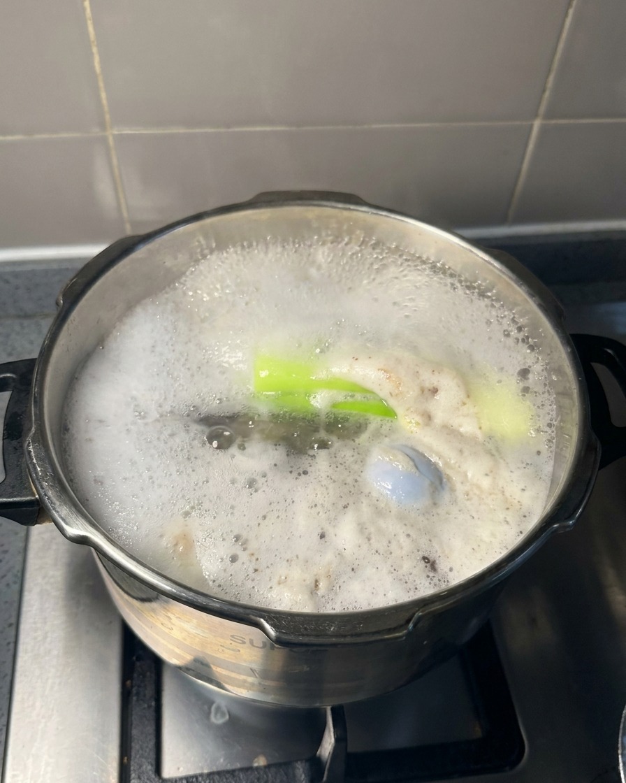 Ein großer Metalllöffel hebt grauen Schaum von der Oberfläche einer kochenden Fleischbrühe ab.