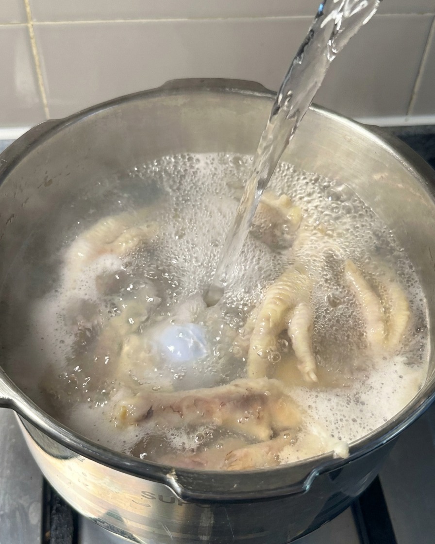 Kochendes Wasser wird in einen Topf gegossen, der bereits vorgegarte Hühnerfüße und Knochen enthält.