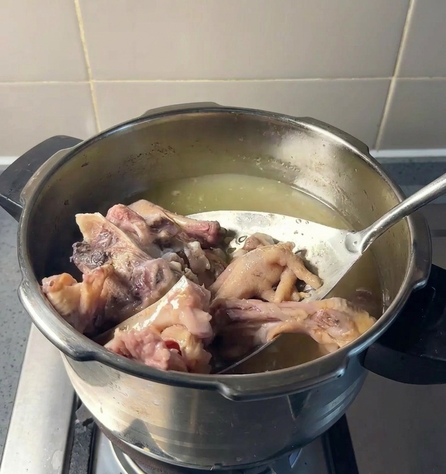 Ein Schaumlöffel hebt Fleisch- und Knochenstücke aus einem Topf mit gelblicher Brühe.