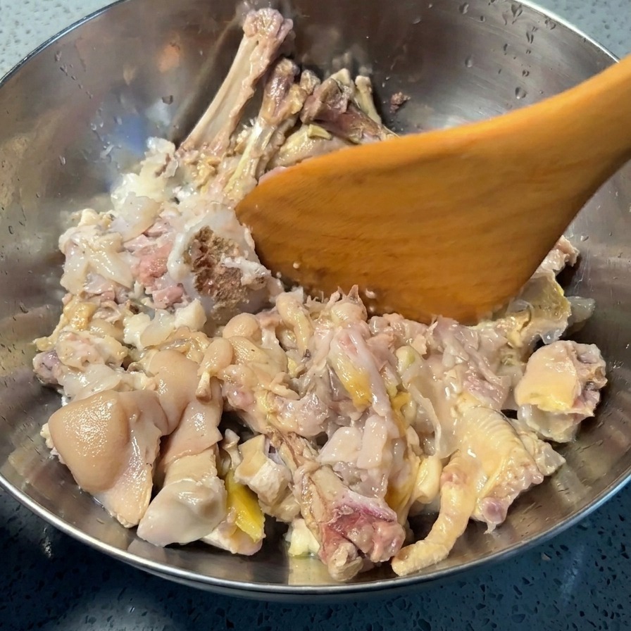 Ein Holzspatel drückt gegarte Fleischteile in einer Schüssel fest, um sie von den harten Knochen zu lösen.