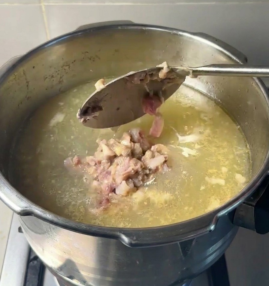 Ein Löffel gibt Klumpen der Fleischpaste zurück in den Topf mit der ursprünglichen Suppenbasis.
