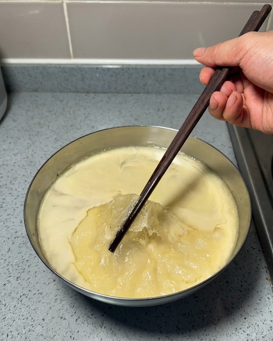 Holzstäbchen heben eine dünne Schicht festen Fetts von einer gelierten Suppenbasis ab.