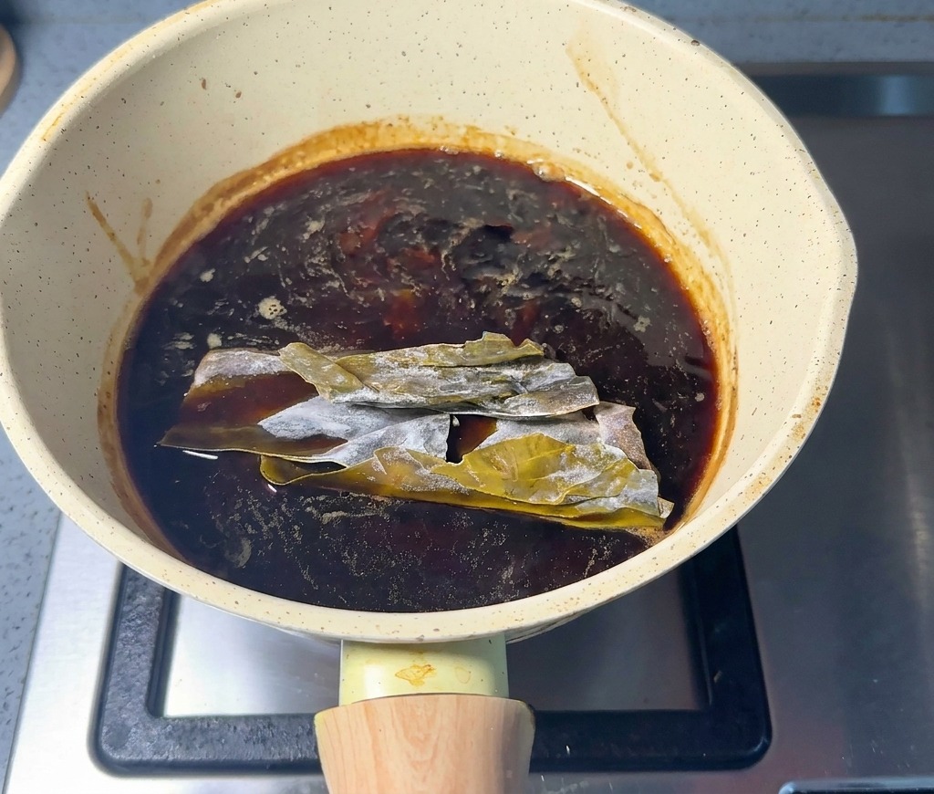 Getrockneter Kombu-Seetang liegt in der dunklen Würzsauce in einem Stieltopf.