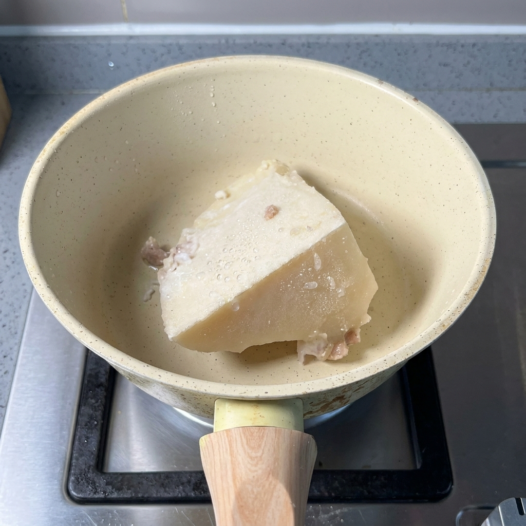 Ein gefrorener Block Schweineknochenbrühe und ein Löffel Fischpulver in einem Topf.