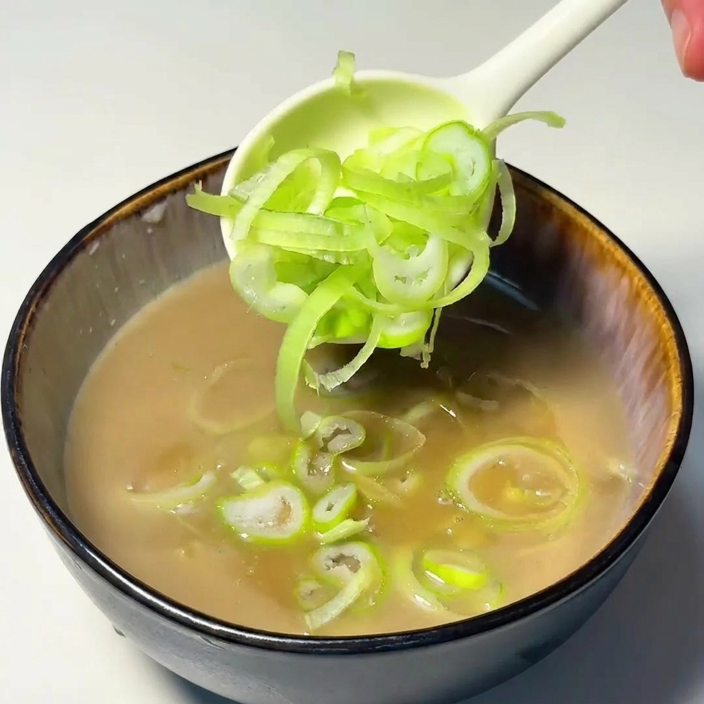 Ein Löffel gibt frisch geschnittene Frühlingszwiebelringe in die Dipping-Suppe.