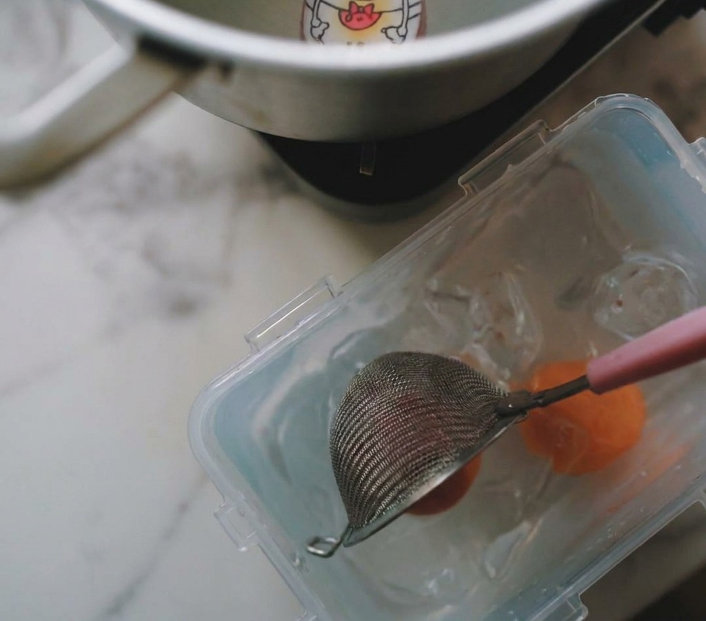 Ein Sieb hebt ein gekochtes Ei aus dem Topf in eine Schale mit Eiswasser.