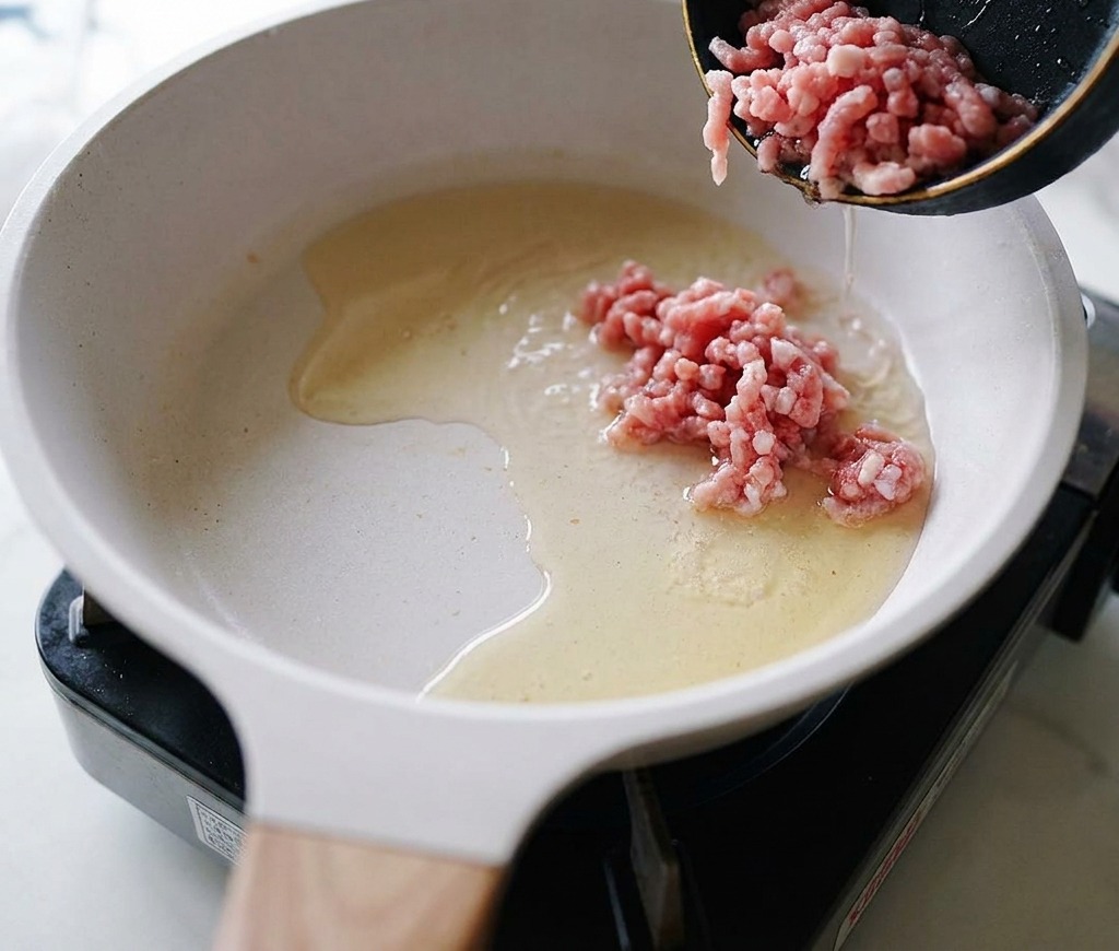 Rohes Schweinehack wird in eine Pfanne mit erhitztem Öl gegeben.