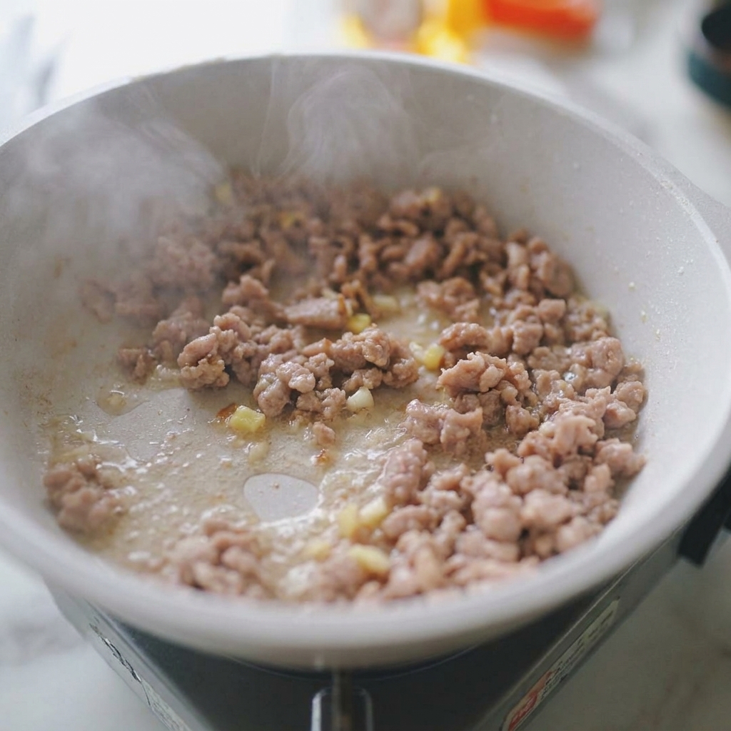 Schweinehackfleisch brät mit Knoblauch und Ingwer in einer hellen Pfanne.