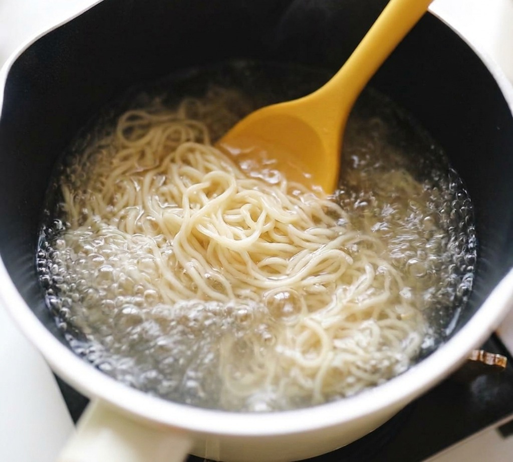 Gelbe Ramen-Nudeln werden in einem Topf mit sprudelndem Wasser umgerührt.