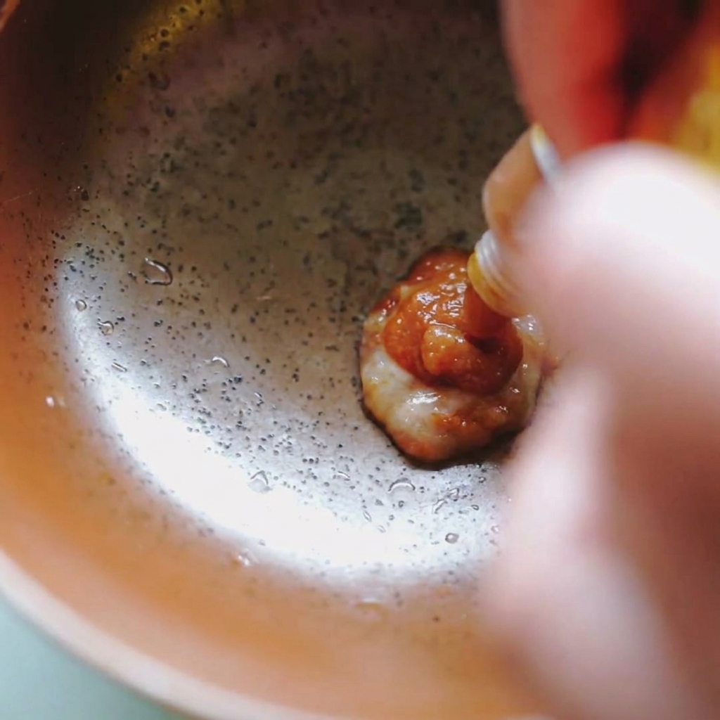Braune Miso-Paste wird aus einer kleinen Packung in eine Keramikschüssel gedrückt.