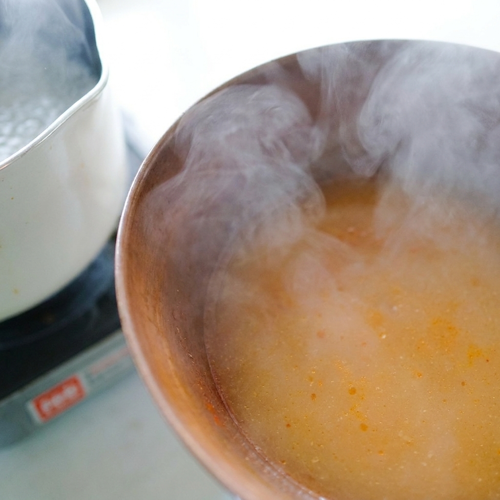 Heißes Nudelwasser wird mit einer Kelle in die Schüssel zur Miso-Paste gegossen.