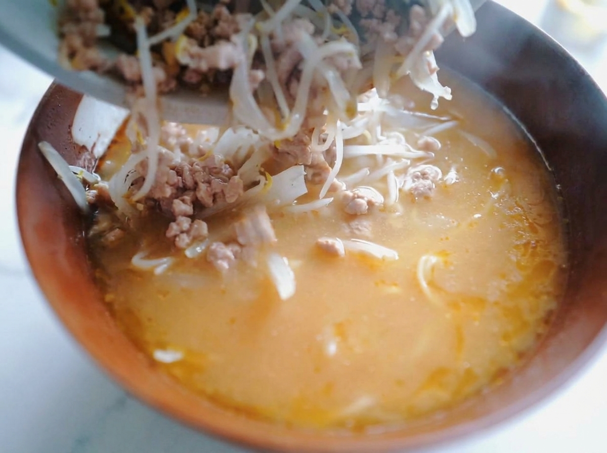 Ein Löffel gibt die Fleisch-Sprossen-Mischung auf die Ramen-Nudeln in der Schüssel.