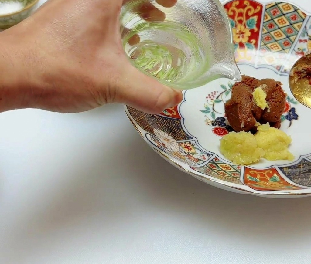 Klares Speiseöl wird aus einem kleinen Glaskännchen über die Miso- und Ingwerpaste gegossen.