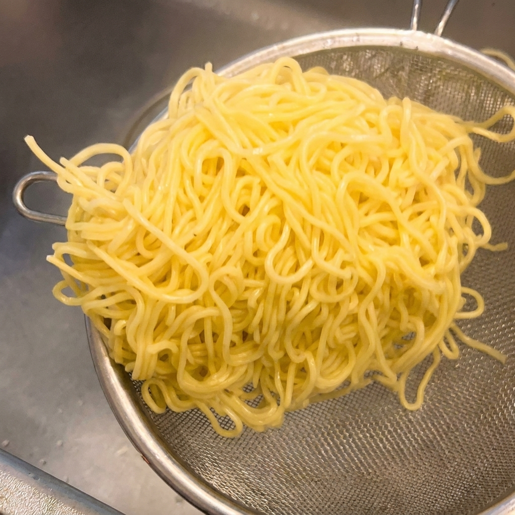 Gekochte gelbe Ramen-Nudeln in einem Metallsieb werden geschüttelt, um überschüssiges Wasser zu entfernen.