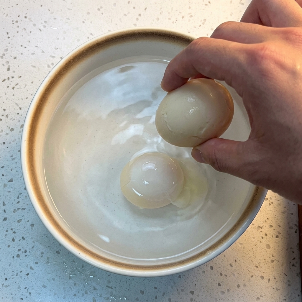 Ein Ei wird in eine weiße Keramikschüssel mit Eiswürfeln und kaltem Wasser getaucht.