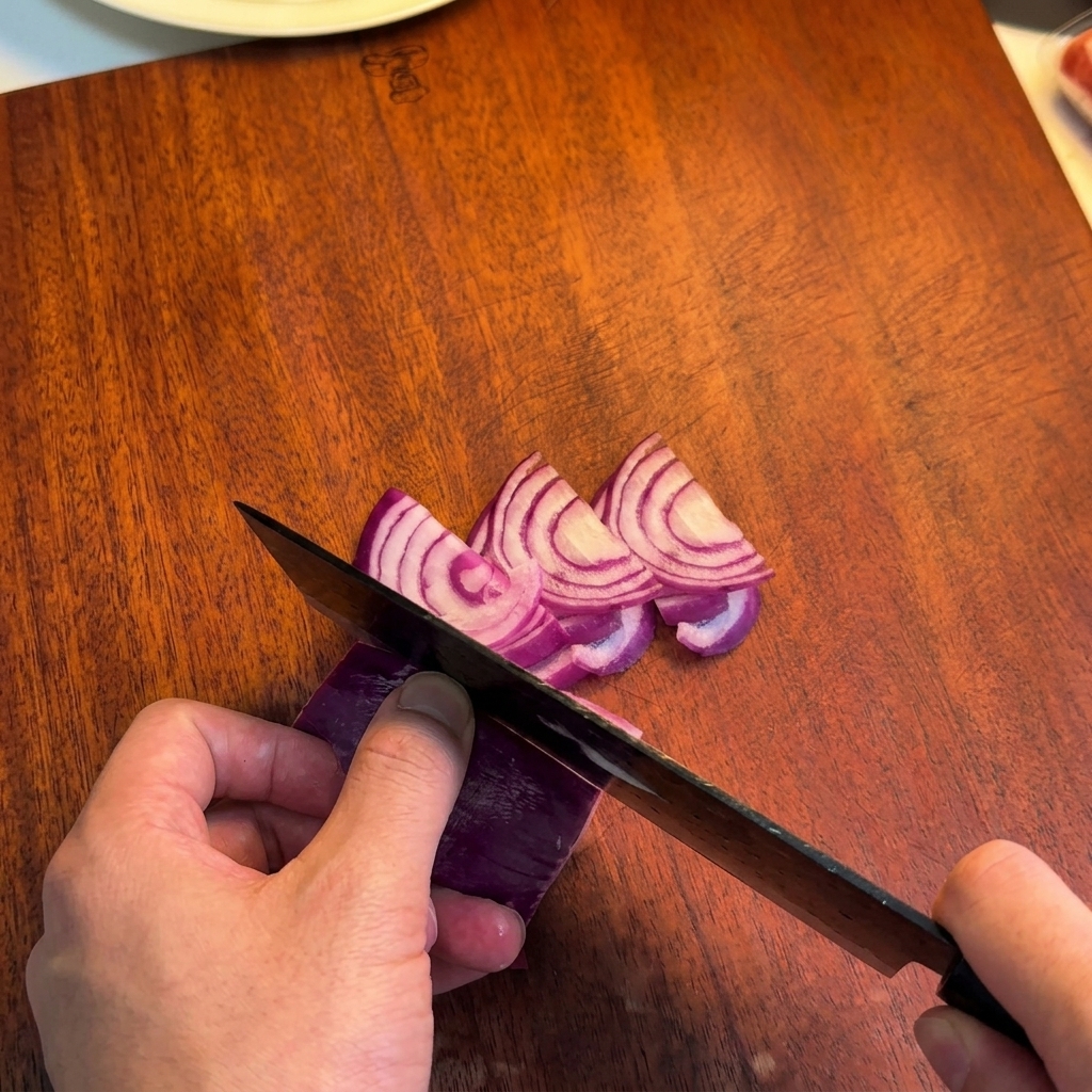 Eine Person schneidet eine rote Zwiebel mit einem Kochmesser in feine Streifen.