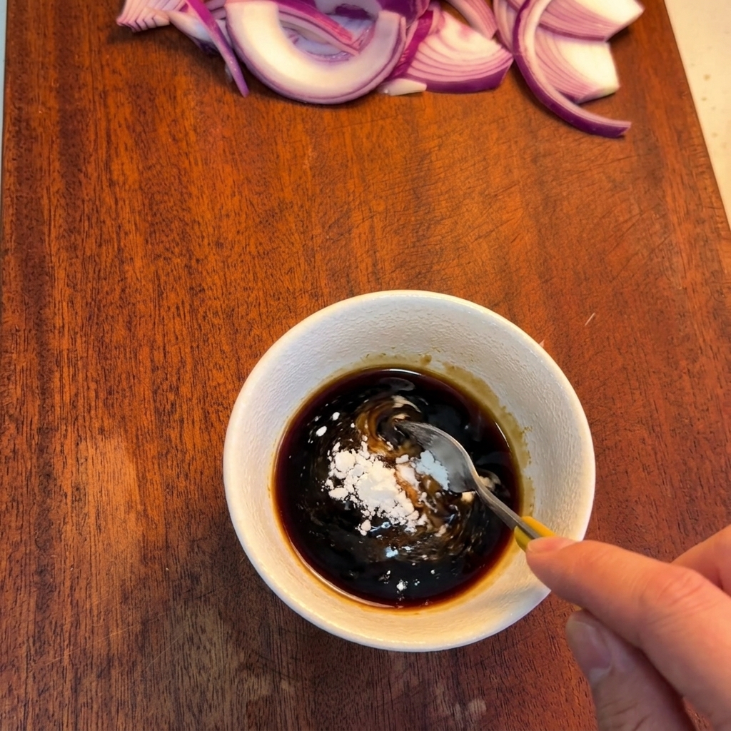 Ein Löffel rührt weiße Stärke in eine dunkelbraune Sauce in einer Schüssel.