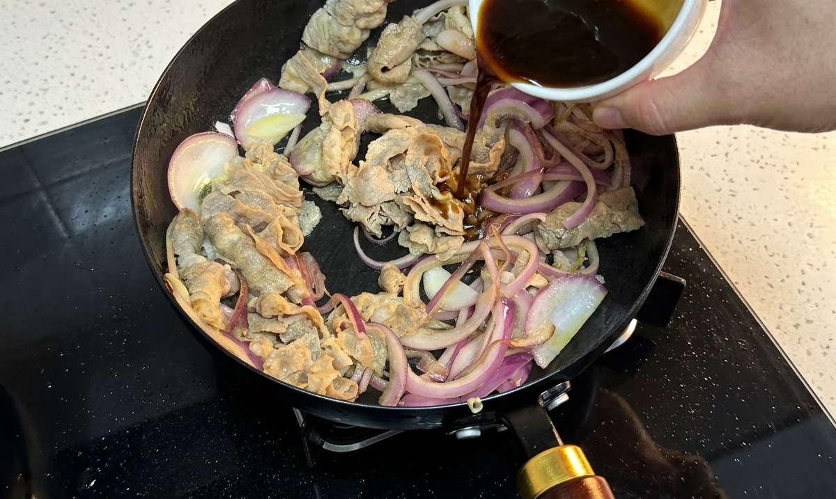 Dunkle Sauce wird über das Rindfleisch und die Zwiebeln in der Pfanne gegossen.