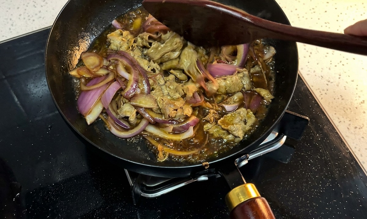 Fleisch und Zwiebeln köcheln in einer dicken dunklen Sauce in der Pfanne.